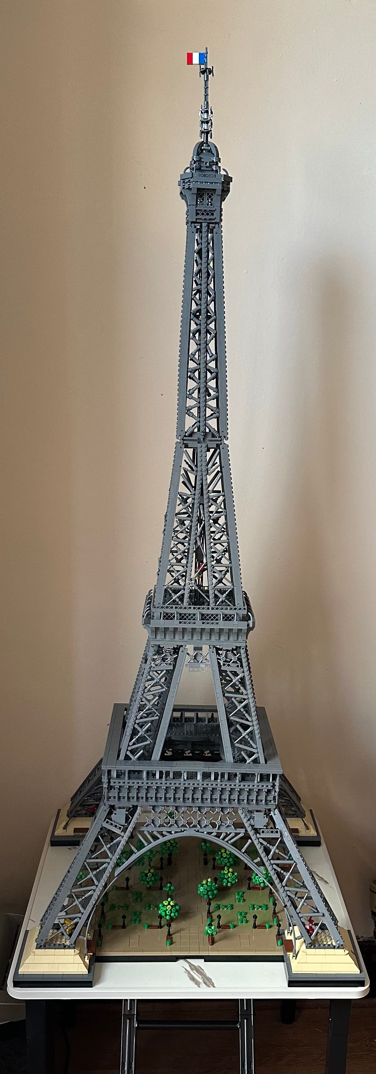 The image shows a Lego Eiffel Tower, standing on a small table. The tower is grey and is very tall.