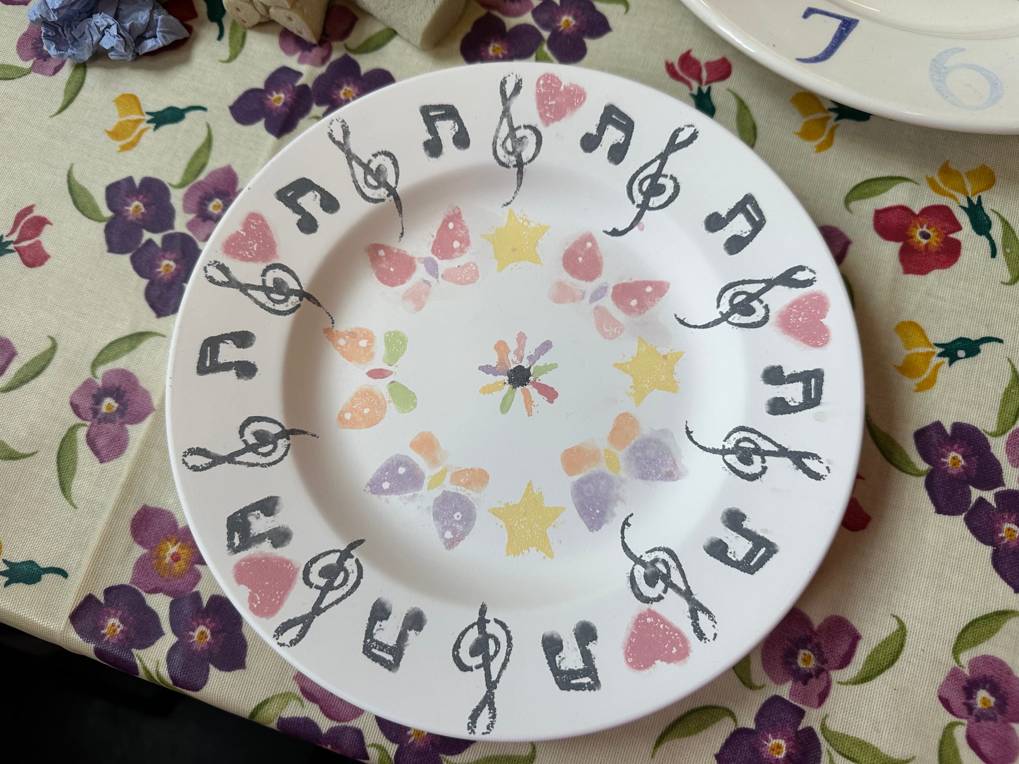 This plate has black treble clefs and musical notes around the edge, with red hearts too. In the middle of the plate are brightly coloured butterflies, with yellow stars
