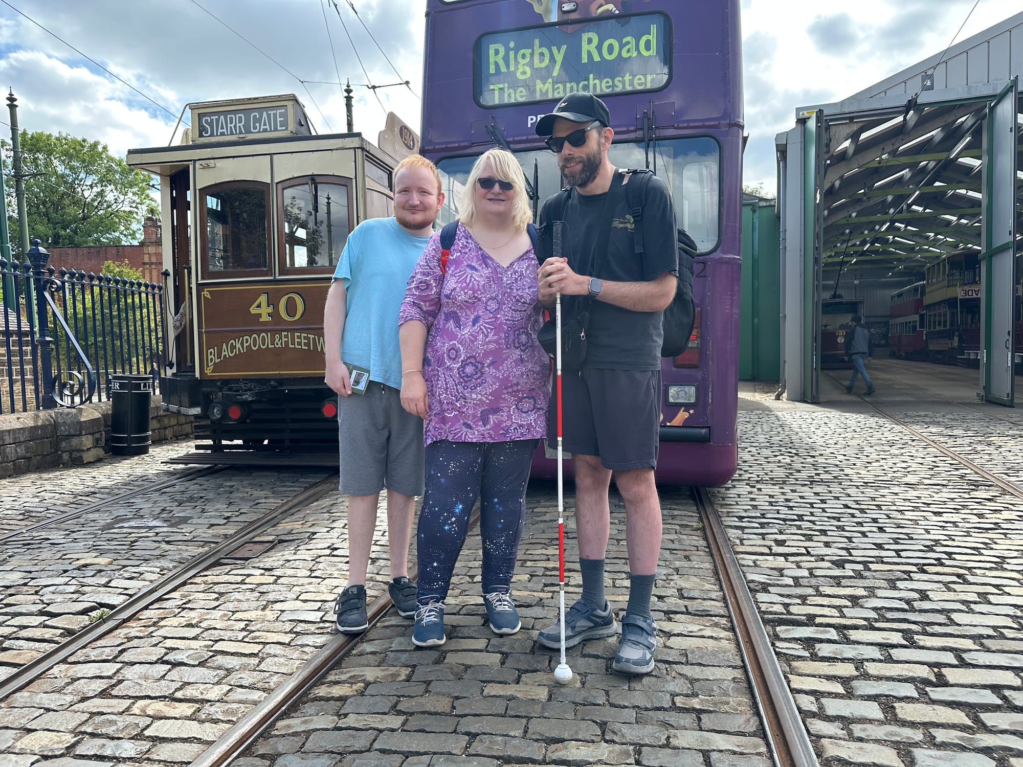The three of us standing between the tramlines and on the cobbles in front of a purple tram. To the left, behind us is an old brown tram that has a destination of Starr Gate on it, and say 40 Blackpool & Fleetwood on the front