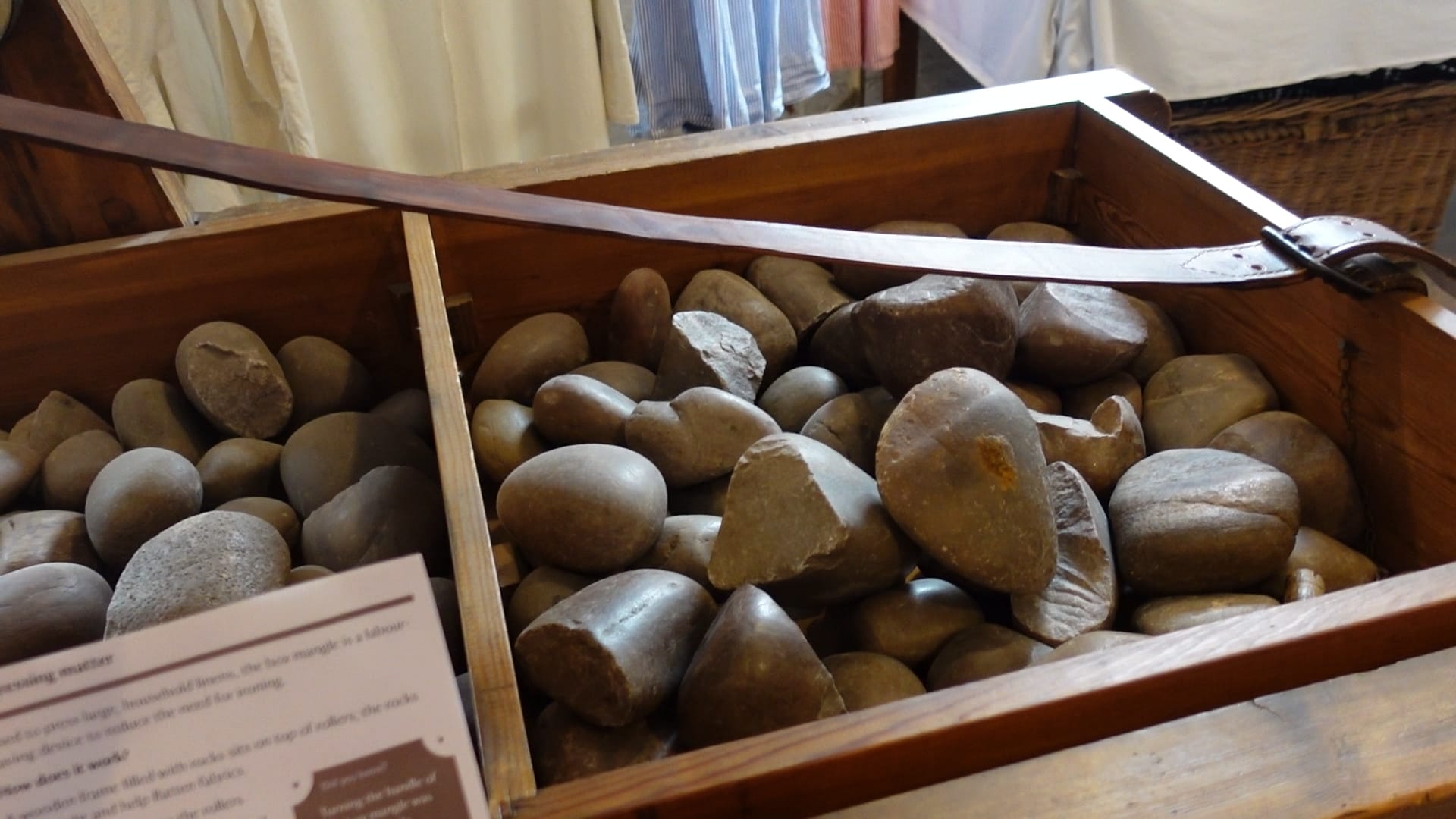 A wooden box, with a divider in the middle, filled with rocks/ A brown strap runs across the top