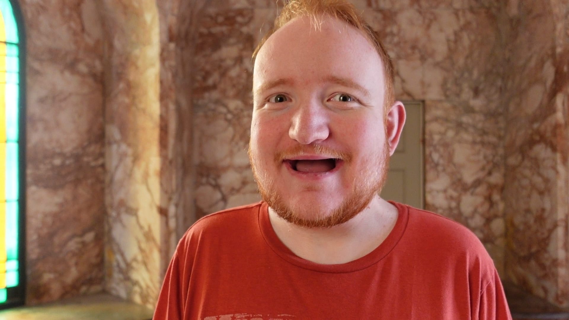 George, a young man in his 20s, stands with a big, open smile in front of the camera