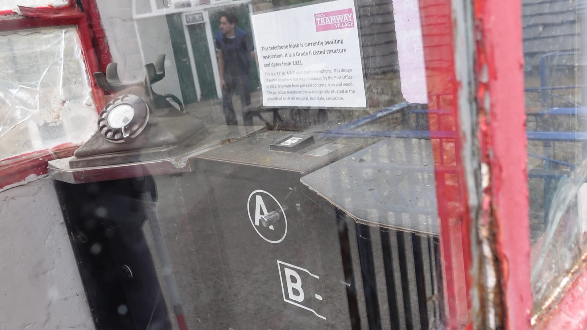 Looking through the glass at the inside of an old phone box. The old rotary dial phone can be seen in the corner, although the receiver appears to be missing, and the A and B payment buttons
