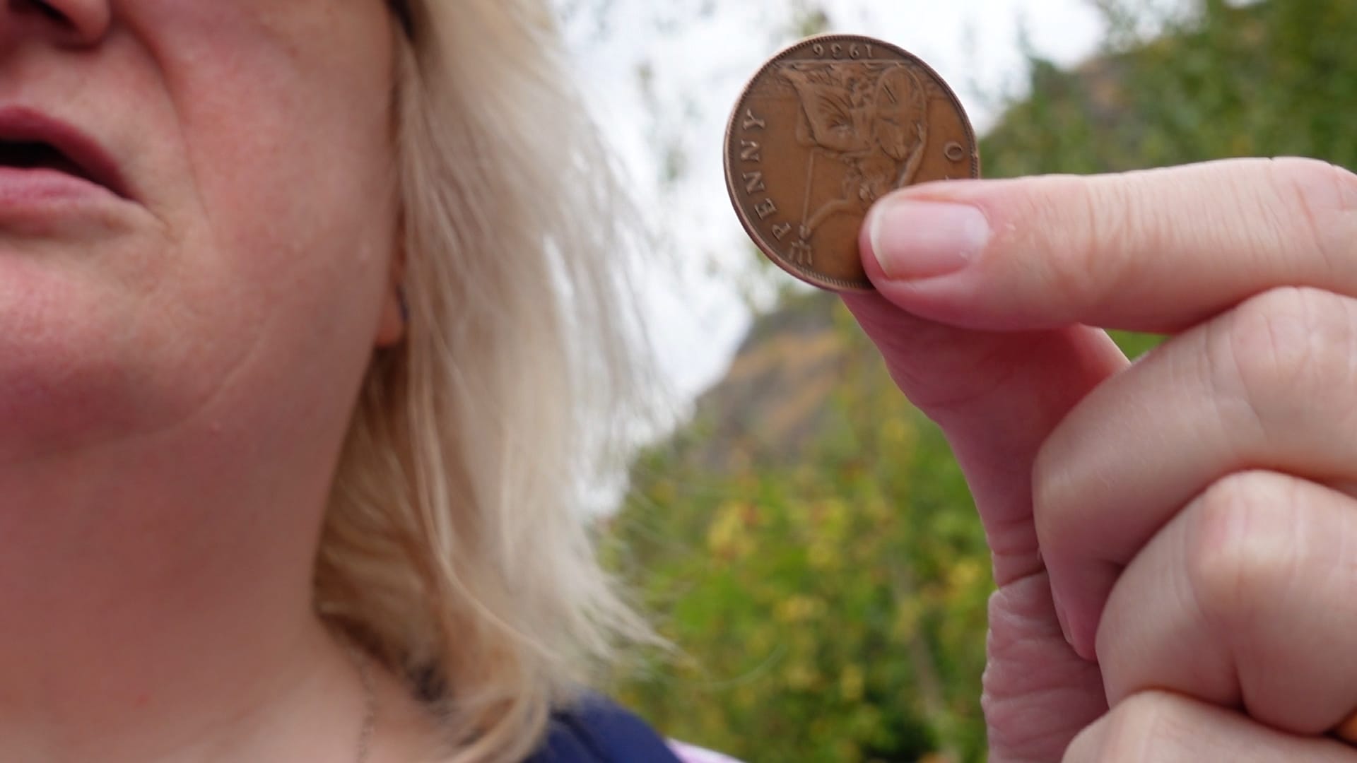 Part of Sue's face is in shot as she holds up an old penny between her thumb and index finger