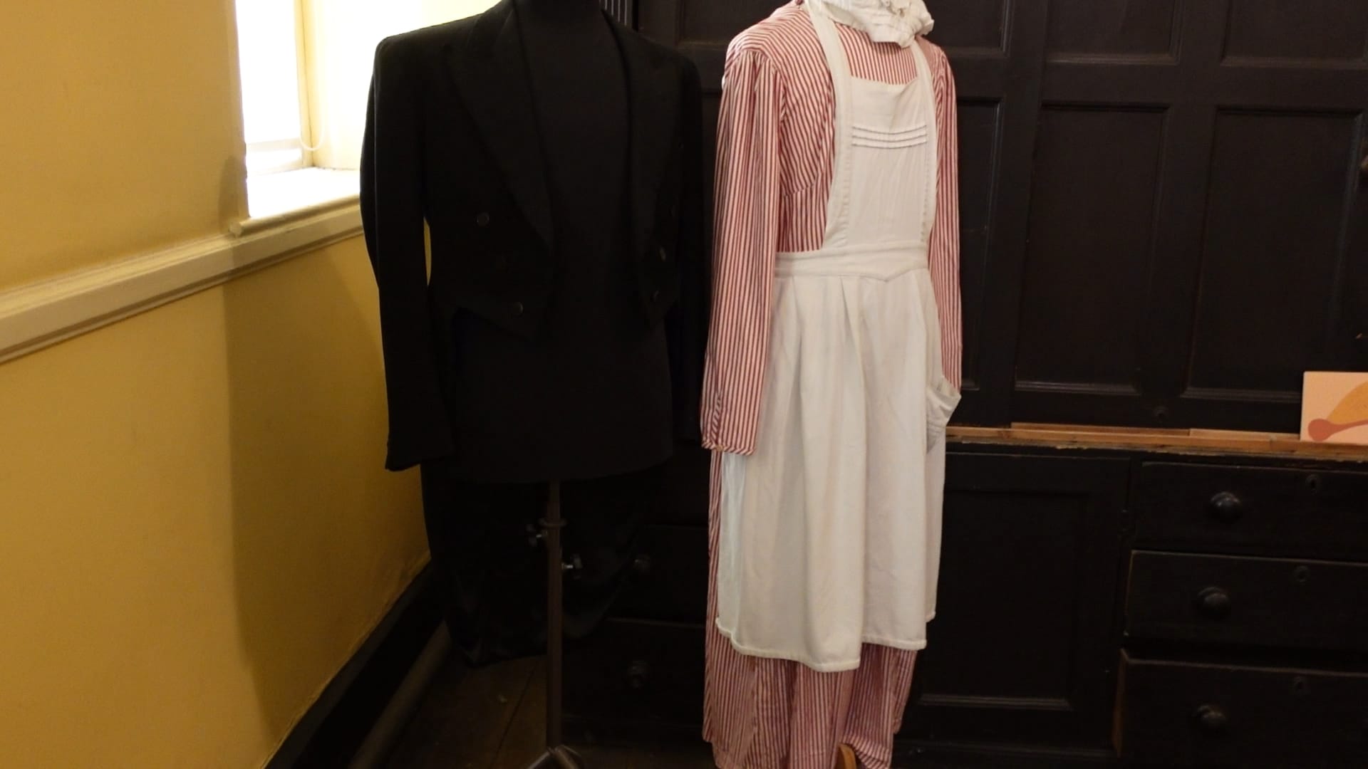 On the left is a black suit, the kind associated with butlers. On the right, a striped red and white dress, with a white apron over it, typically associated with maids