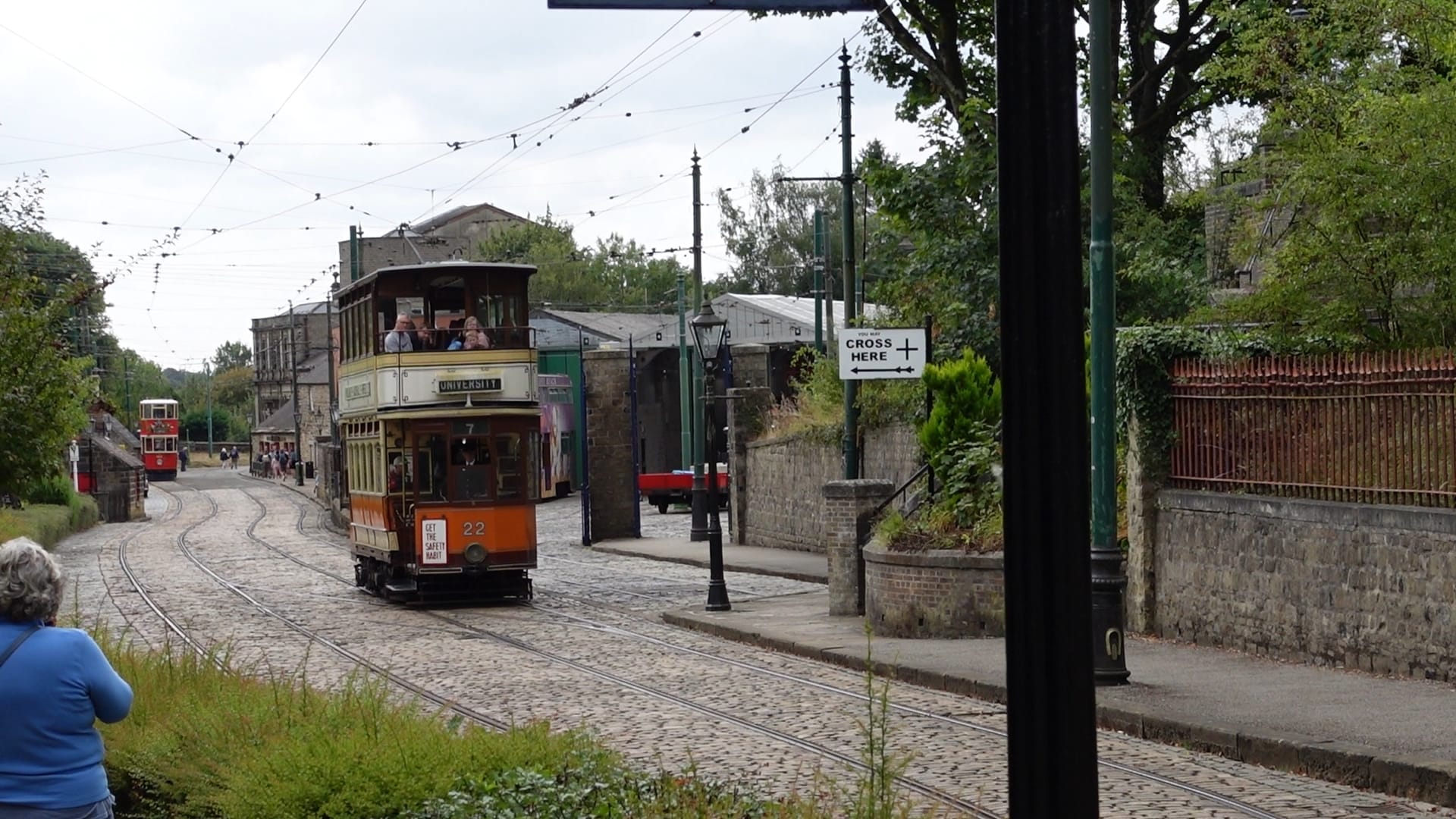 A cobbled street with tramlines on it. A double decker tram approaches. It is orange on the bottom and white at the top. It's destination shows University.