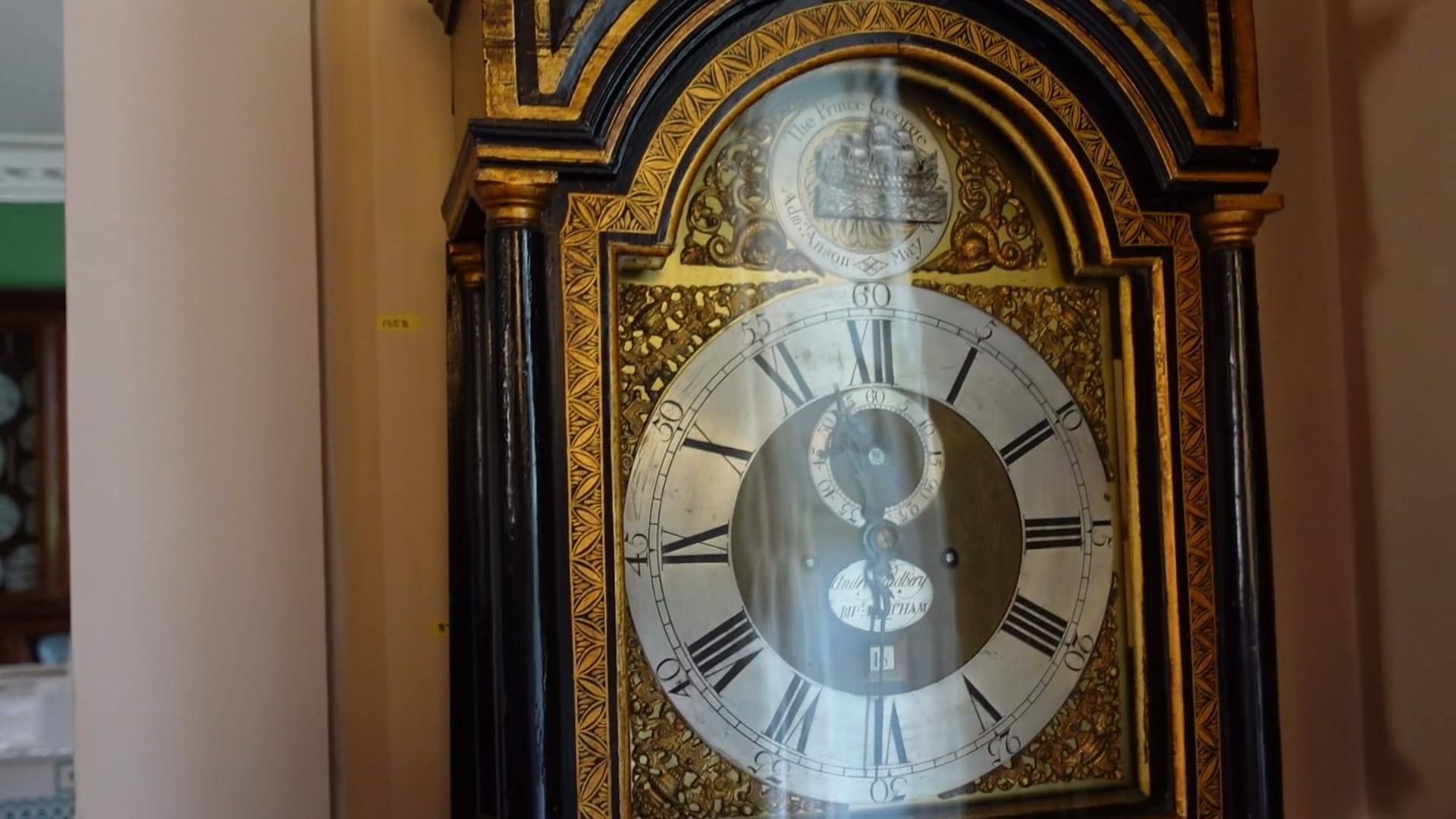 A close up of the face of a grandfather clock. Above the face there is a ship that moves from left to right to indicate seconds.