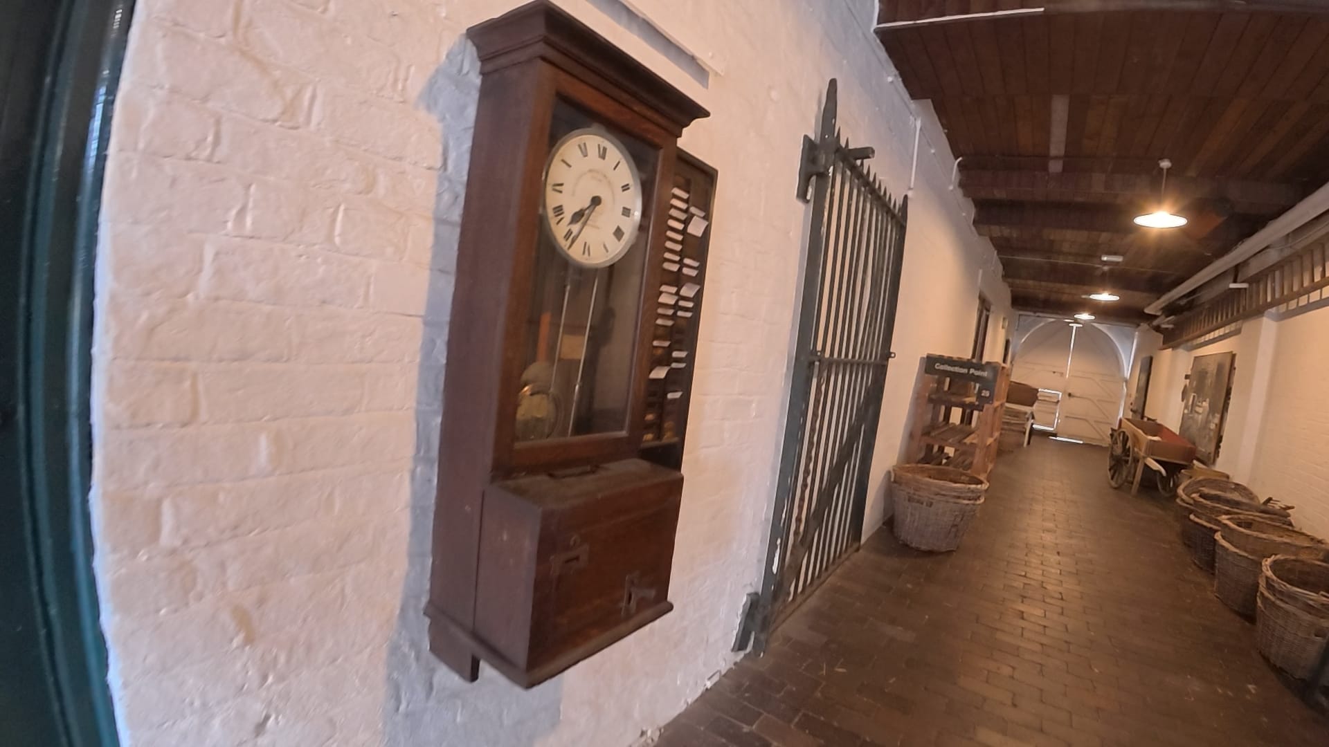 Wooden Victorian clocking-on machine beside iron gates in the entrance passage at Gladstone Pottery Museum.