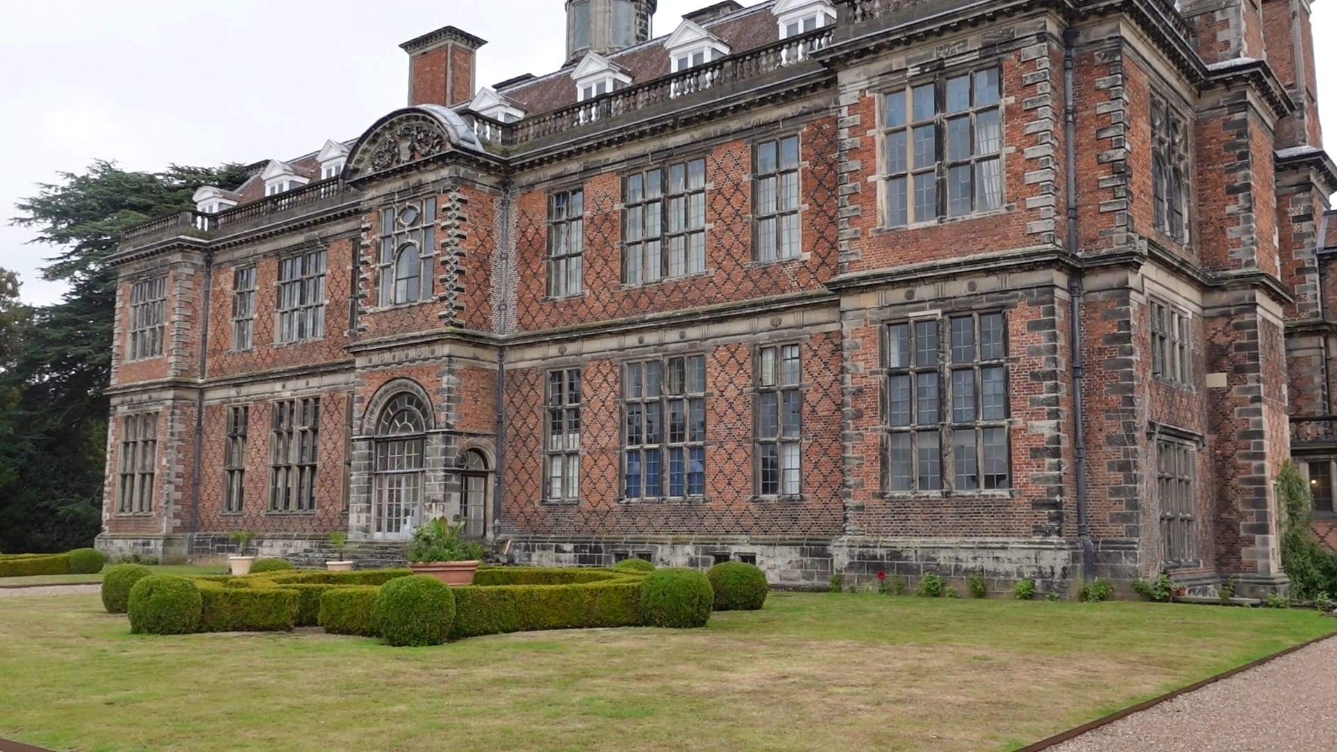 The back of a very large and grand looking country house. It has three floors, that are in view, and lots of windows.