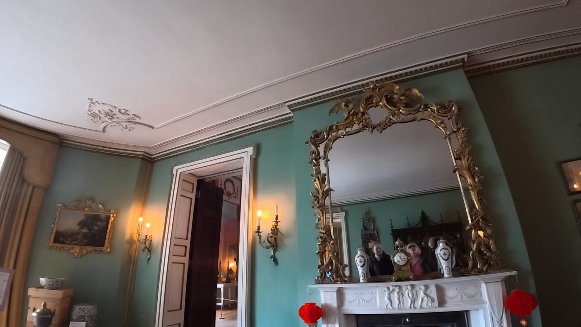 A huge ornate mirror over a fireplace. The reflection shows Sue, John and George