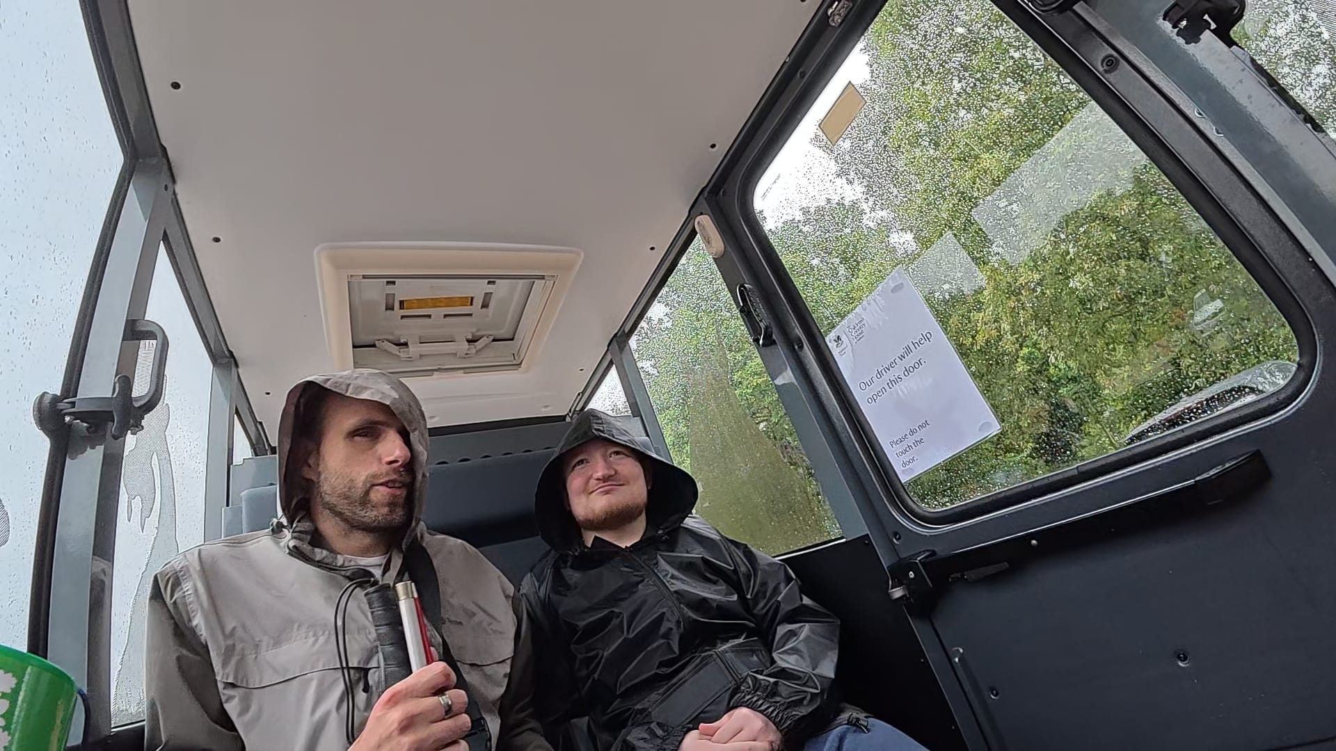 John and George are sitting next to each other onboard the accessible vehicle, Archie, that runs between the car park and the country house.