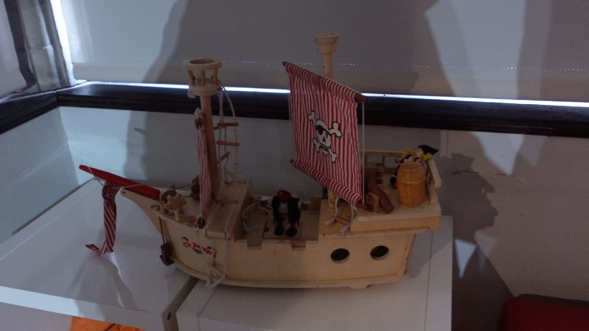 A wooden pirate ship, with a red and white striped sail, and a skull and crossbones emblem in the middle if it.