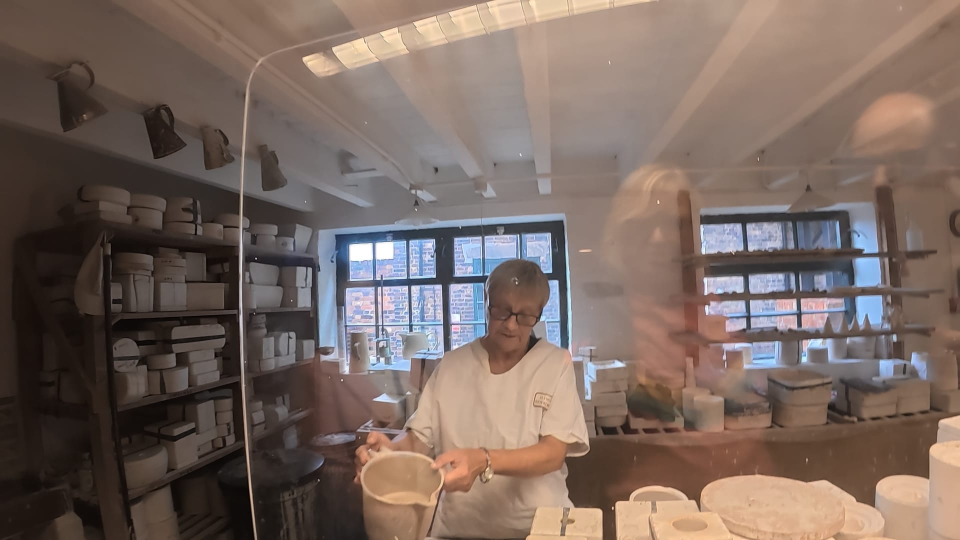 A woman is holding a jug of slip and is about to pour it into a casting mould.