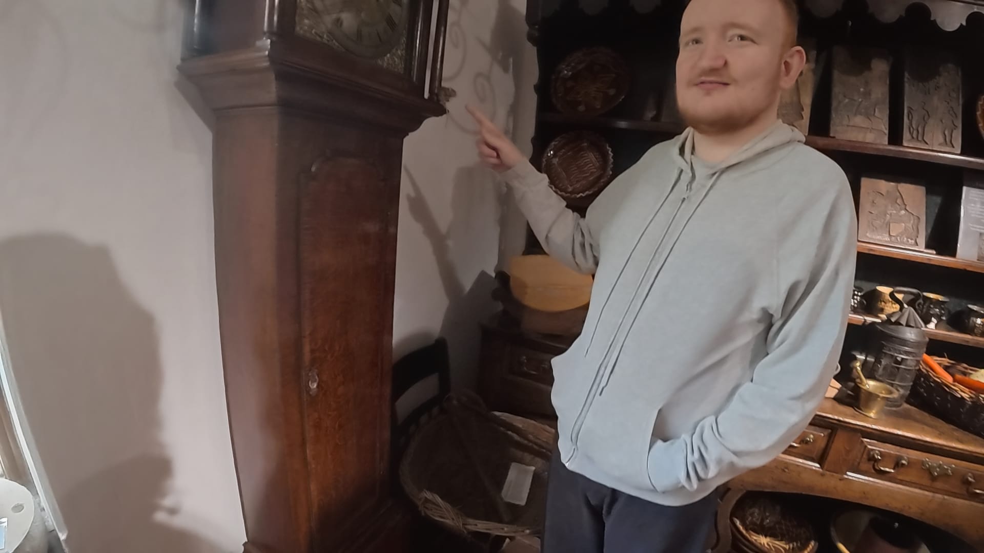 A grandfather clock is to the left. George is in front of it, standing side on, and pointing to a small toy mouse, near to the clock face.