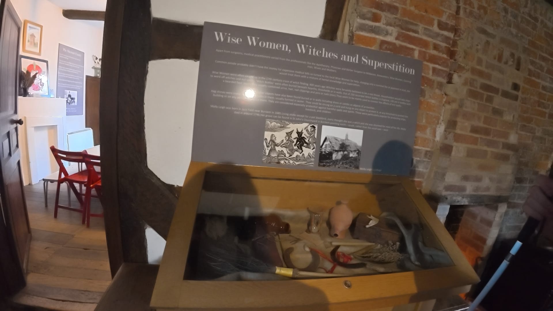 A display cabinet full of items supposed to protect against witches. A grey sign above says "Wise Women, Witches and Superstition." Underneath the title are descriptions of how the items in the case were used.