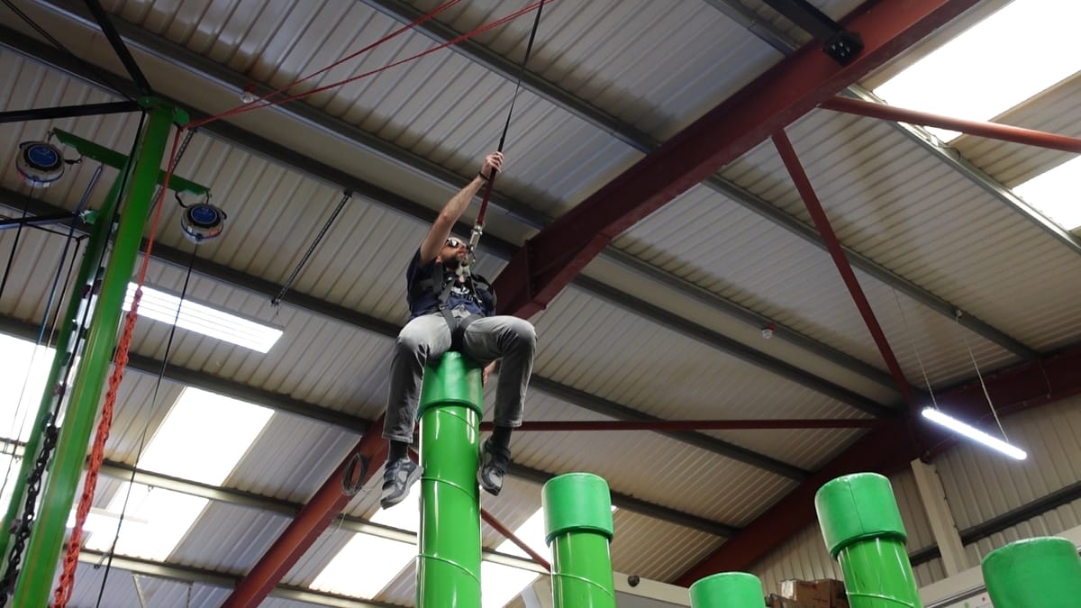 John is sitting on top of a green pole, holding onto a rope in front of him