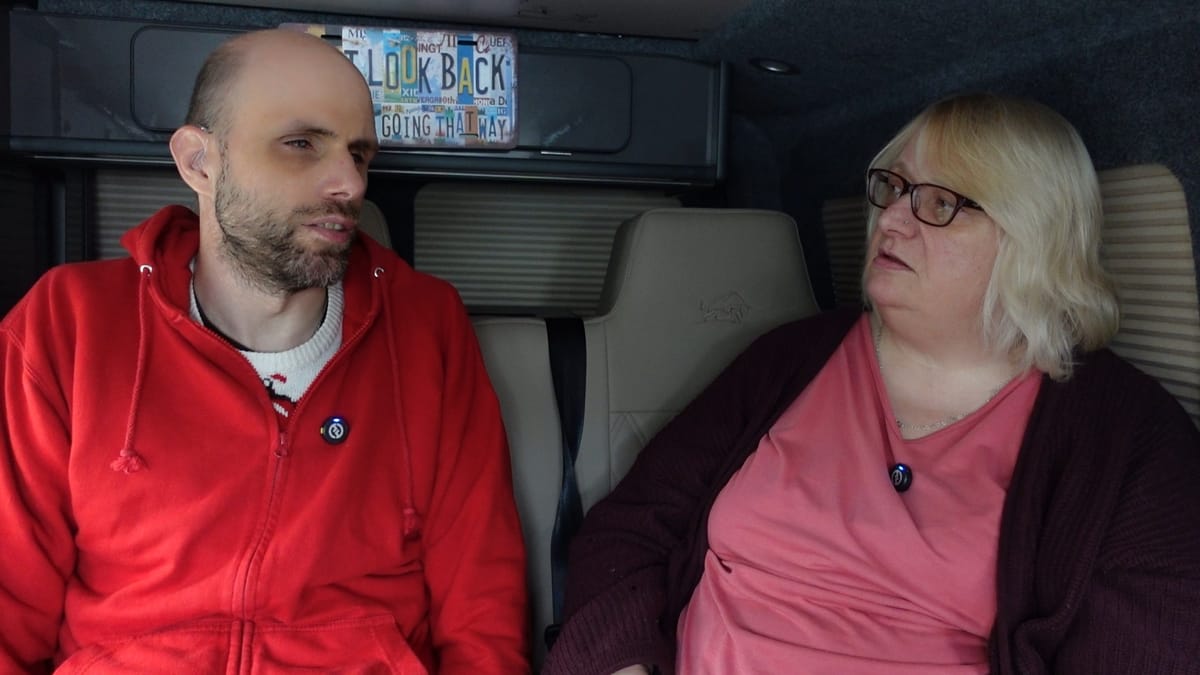 John on the left and Sue on the right, in the camper van. John is talking and Sue listening