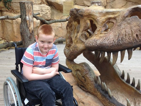 George sitting in a wheelchair, next to a dinosaur head